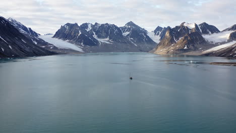 Boat Cruising In The Fjord With Calm Waters Surrounded By Snowy Mountains In Svalbard, Norway. - aerial shot