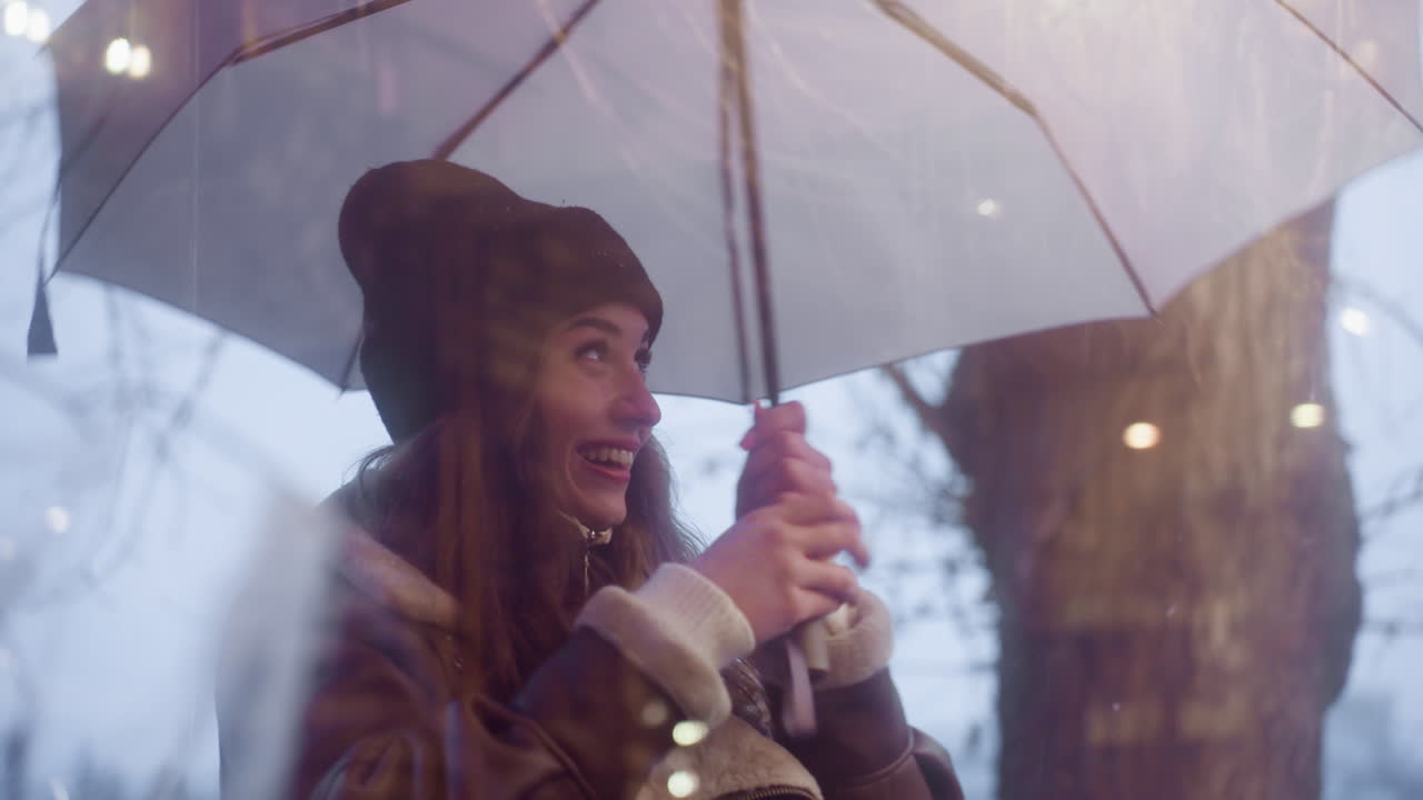 Happy girl holding umbrella, walking past cafe, looking through glass window, laughing, and making peace sign with her finger on cold overcast day, with a joyful expression