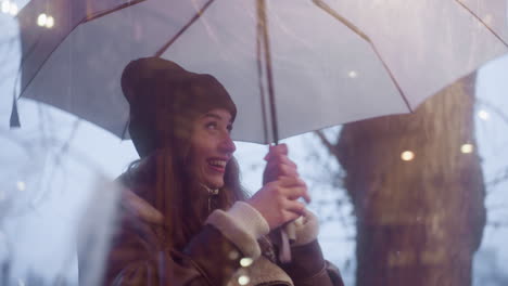happy girl holding umbrella, walking past cafe, looking through glass window, laughing, and making peace sign with her finger on cold overcast day, with a joyful expression