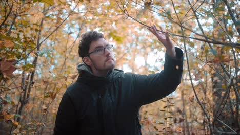 cámara lenta inmersiva de un joven masculino europeo, adornado con barba y gafas, navegando atentamente por la maleza de un bosque mixto durante la vibrante temporada de otoño en alemania