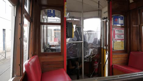 commute inside of historical lisbon tram .vintage wooden cabin interior and red seats. driver cockpit at the front moving control handle. big wheel on his side and fire extinguisher.