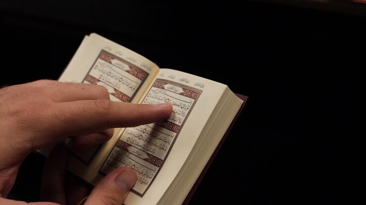 Footage of a man reading the short verses from the noble Quran, the Quran is in the left down corner isolated on a black background