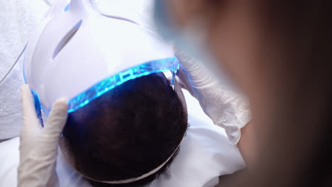 beautiful slow motion long shot of a nurse putting a led mask on a young man lying on a stretcher in a dermatology clinic during a beauty treatment