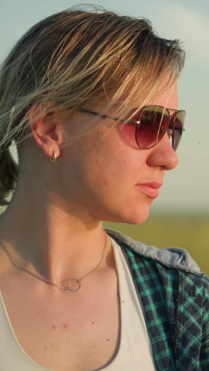 молодая женщина в клетчатой рубашке и солнцезащитных очках всматривается в расстояние, а фон красиво размыт