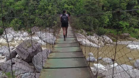 POV-follows-female-hiker-crossing-suspension-foot-bridge-over-river