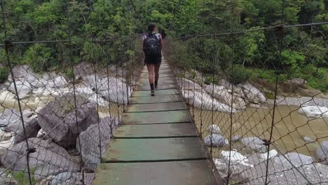 pov follows female hiker crossing suspension foot bridge over river