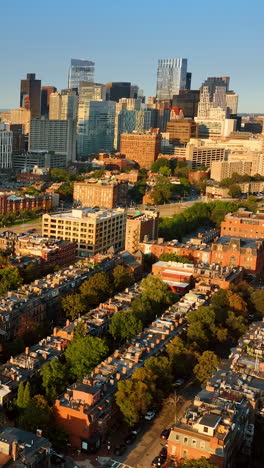 approaching tower blocks flying above the low-rise buildings. sun lighting the facades of the architecture in boston at sunset. top view.. vertical video