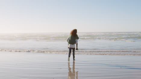 rear view of man giving woman piggyback on winter beach vacation