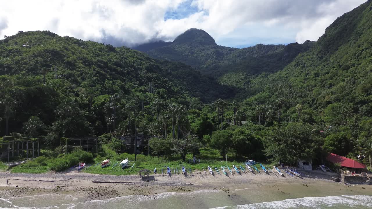 Vídeo aéreo con drones de barcos descansando en la playa Aninuan en Puerto Galera, Filipinas, con agua cristalina, playa de arena, bosque denso y montañas verdes al fondo, formando un paisaje tropical