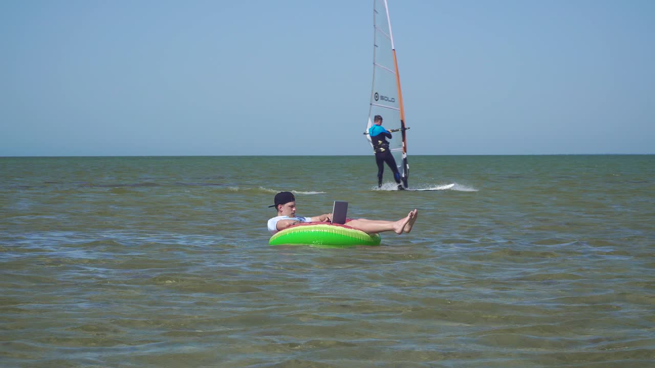 un joven empresario está trabajando con entusiasmo detrás de una computadora portátil balanceándose en las olas del mar