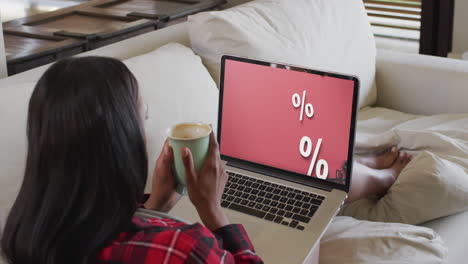 biracial woman using laptop on couch at home online shopping during sale, slow motion