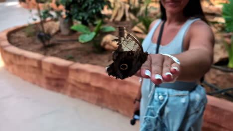 a woman holds a butterfly on her hand in an indoor garden