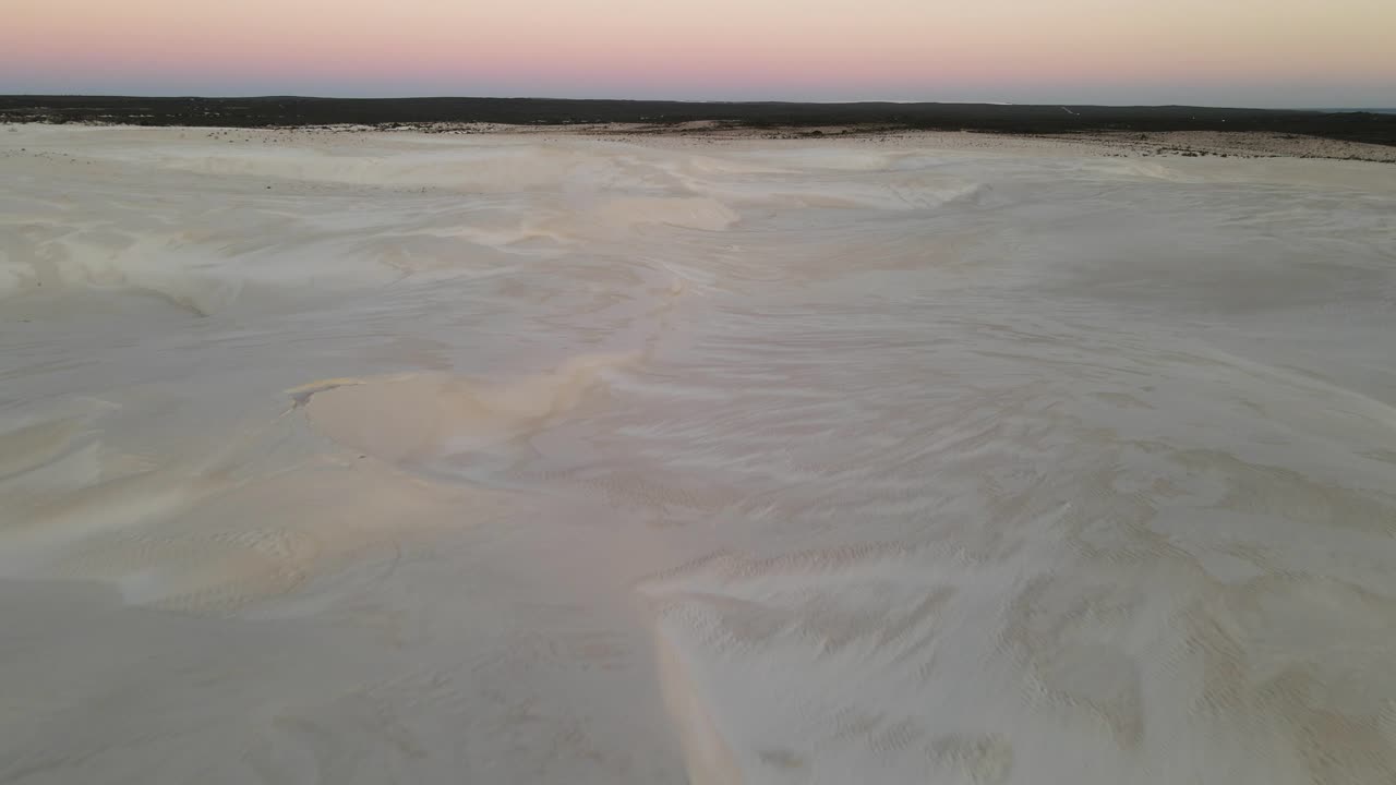 Flying towards landscape photographer with drone in sandunes at sunset in desert