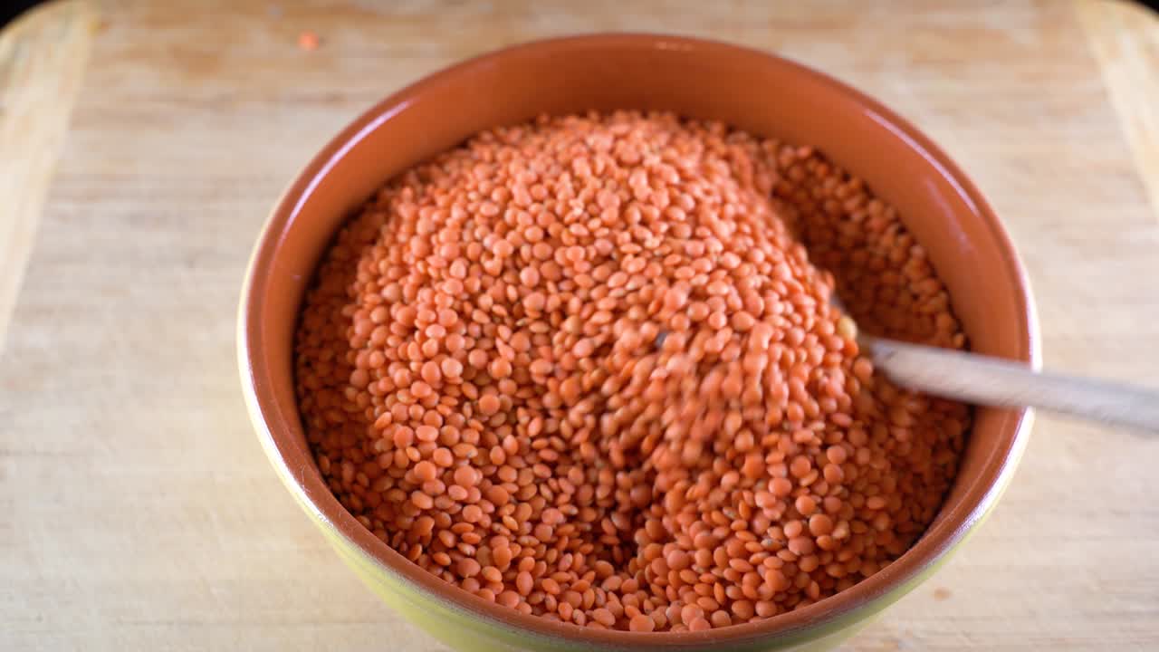 Red lentils in a bowl are sorted with a wooden spoon. High-protein legumes, beans and lentils for a healthy diet.