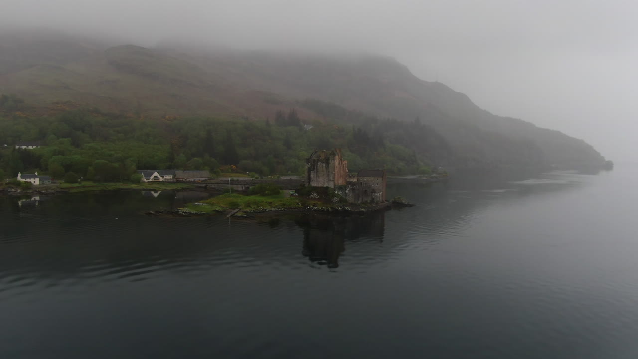 Misty low fog gradually enveloping iconic Eilean Donan Castle, revealing dramatic Scottish Highland landscape with ethereal atmospheric conditions