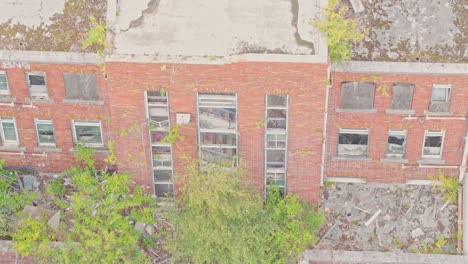 drone ascends past the facade of the abandoned salford crescent police station. the red-brick building shows broken windows, boarded openings, and vegetation sprouting from its roof and walls