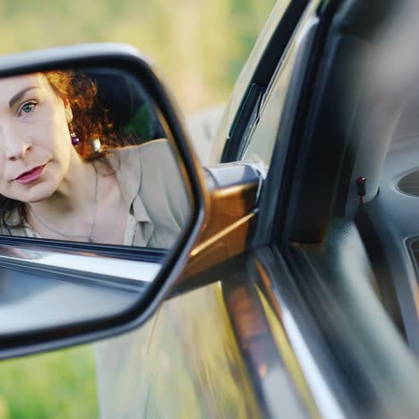 beautiful brunette woman looking at sideview mirror preening her hair before driving car close up