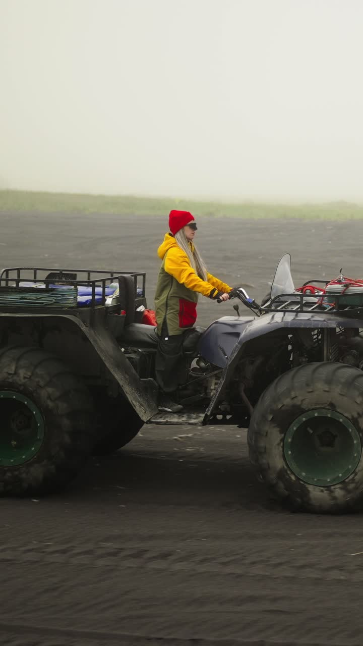 Donna che guida un quad su una spiaggia di sabbia nera con tempo nebbioso