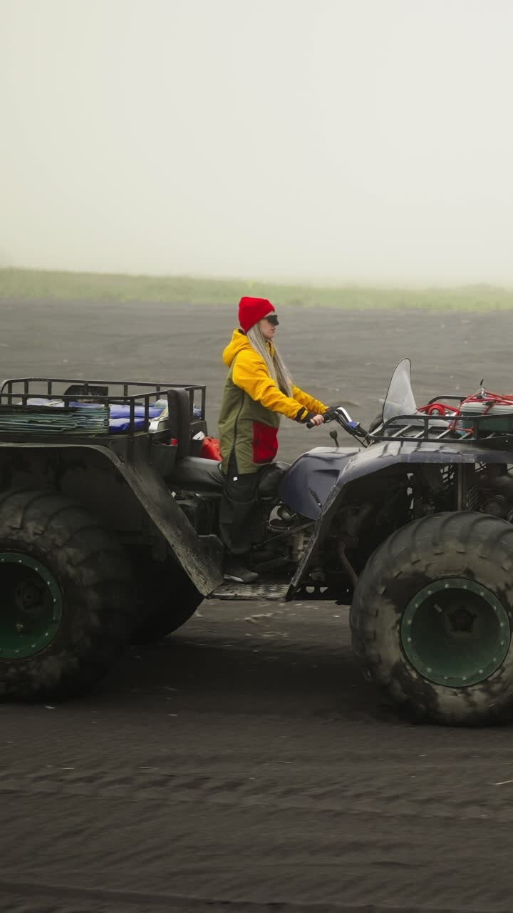 Donna che guida un quad su una spiaggia di sabbia nera con tempo nebbioso