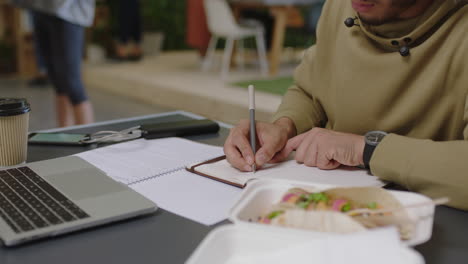 joven estudiante de negocios árabe tormenta de ideas escribiendo notas disfrutando de estudiar usando portátil investigando en línea escuchando música en una oficina ocupada lugar de trabajo de cerca