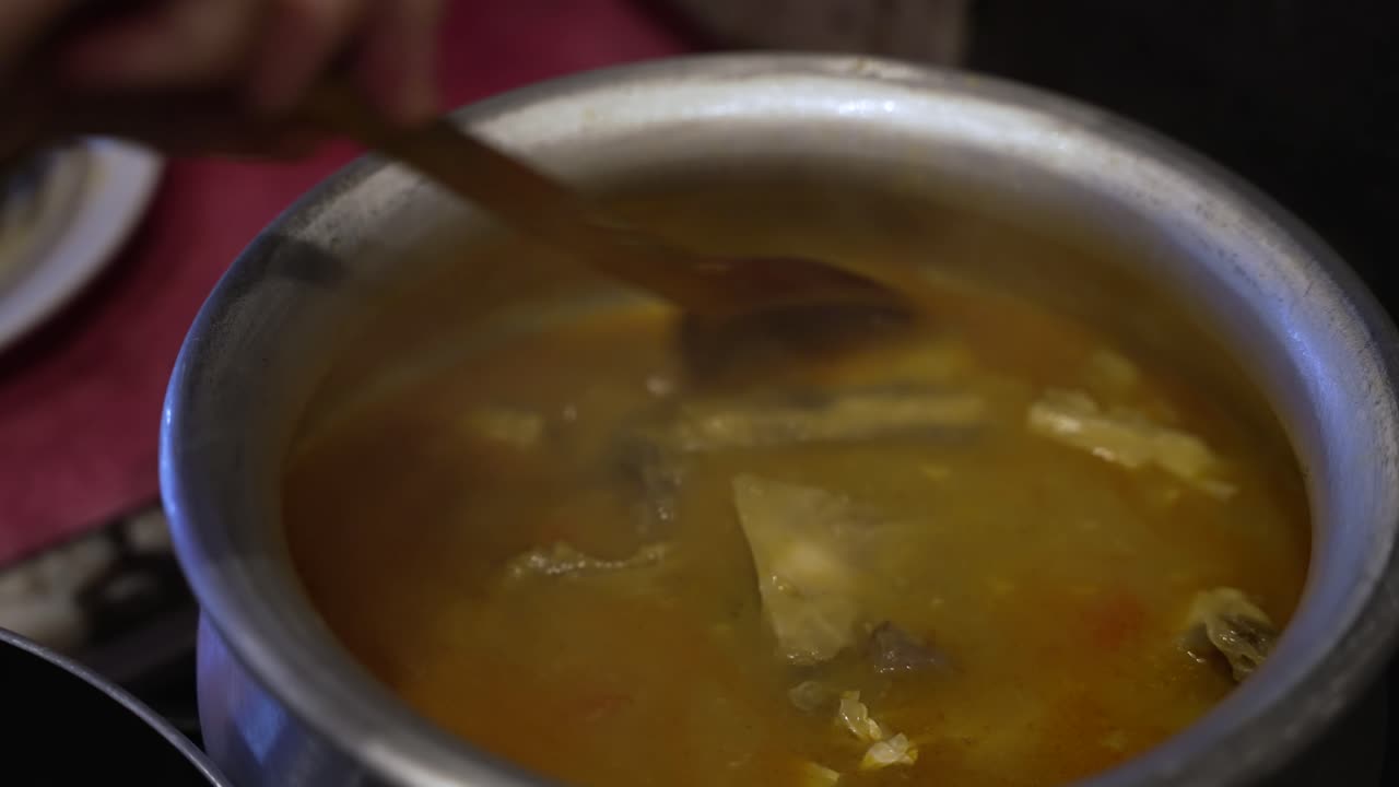 vista de cerca del curry de pescado bengalí con tomates revueltos en una olla de metal con una cuchara de madera