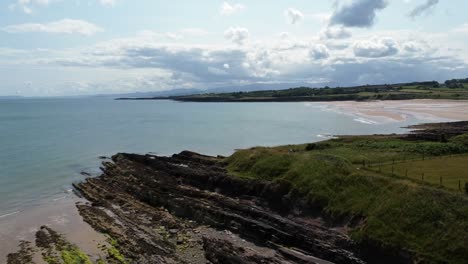 Traeth-Lligwy-idyllic-rocky-coast-shoreline-aerial-view-green-pasture-on-rocky-cliffs-edge,-rising-right-shot