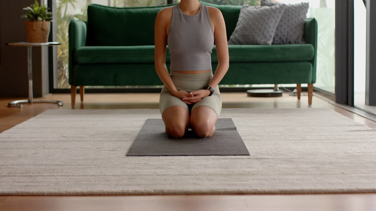 Kneeling on yoga mat, woman meditating and relaxing in living room, at home