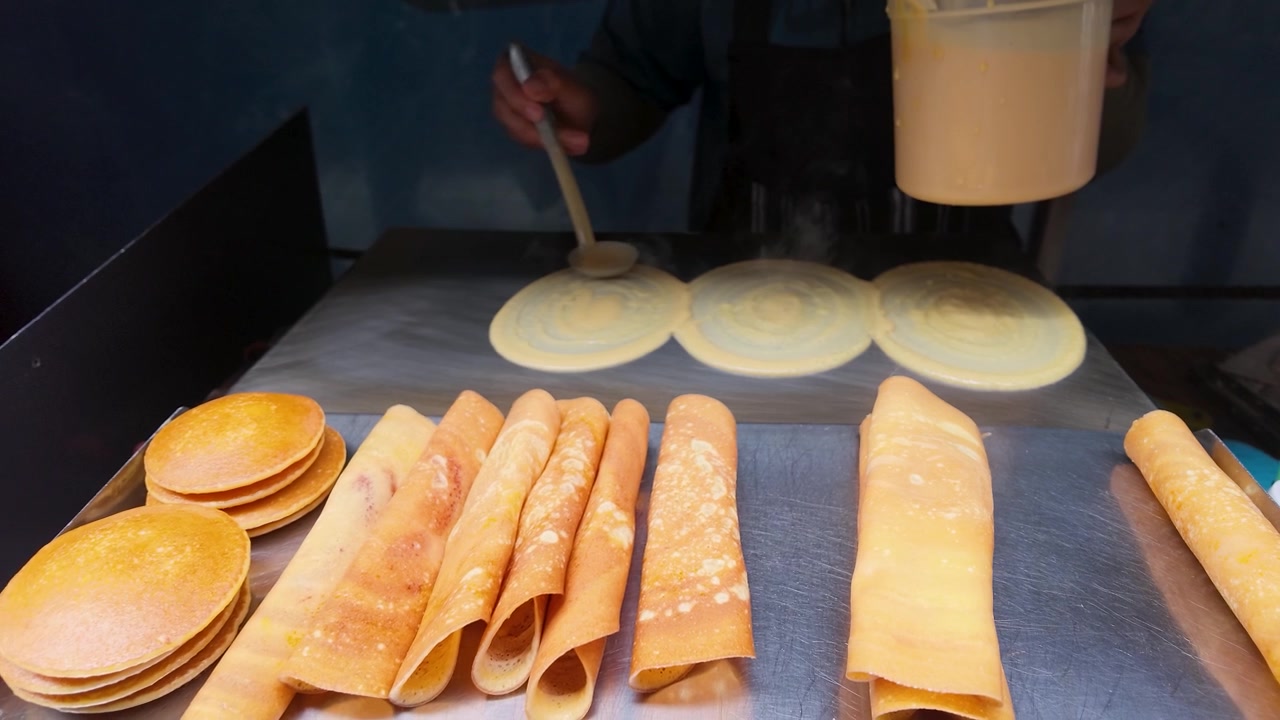 Close-up shot of a vendor spreading batter to cook thin pancakes at a market.