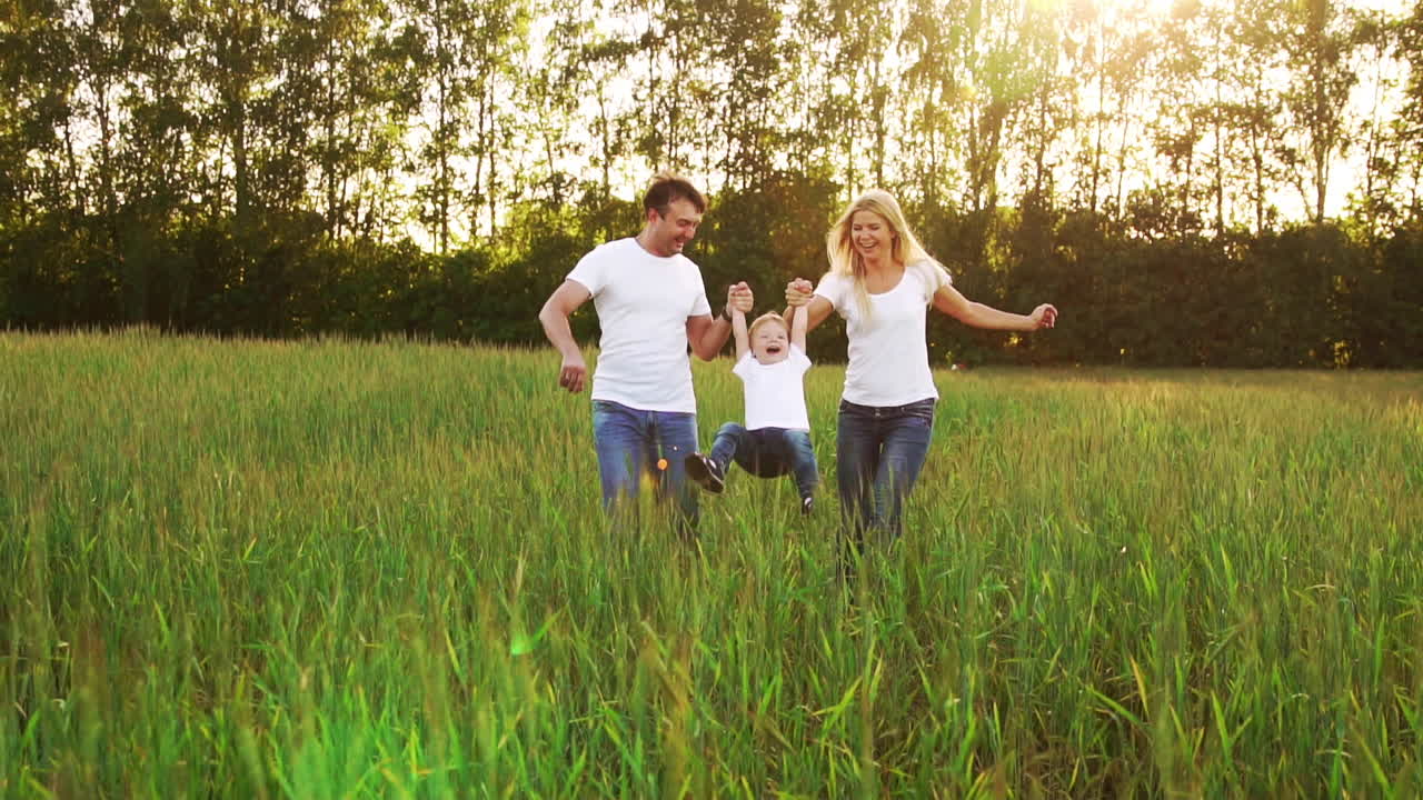 familia feliz: padre, madre e hijo, corriendo en el campo vestidos con camisetas blancas