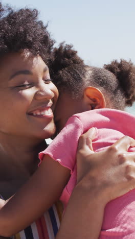 sonriente madre afroamericana con su hija abrazándose en una playa soleada