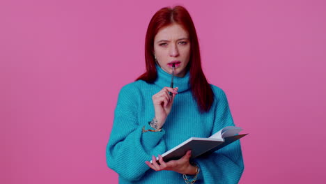 pensive ginger woman making notes, writing down thoughts with pen into notepad notebook diary indoor