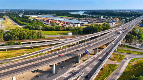 European industrial highway interchange. Vehicles travel along a complex highway interchange near a bustling industrial area with a river in the distance