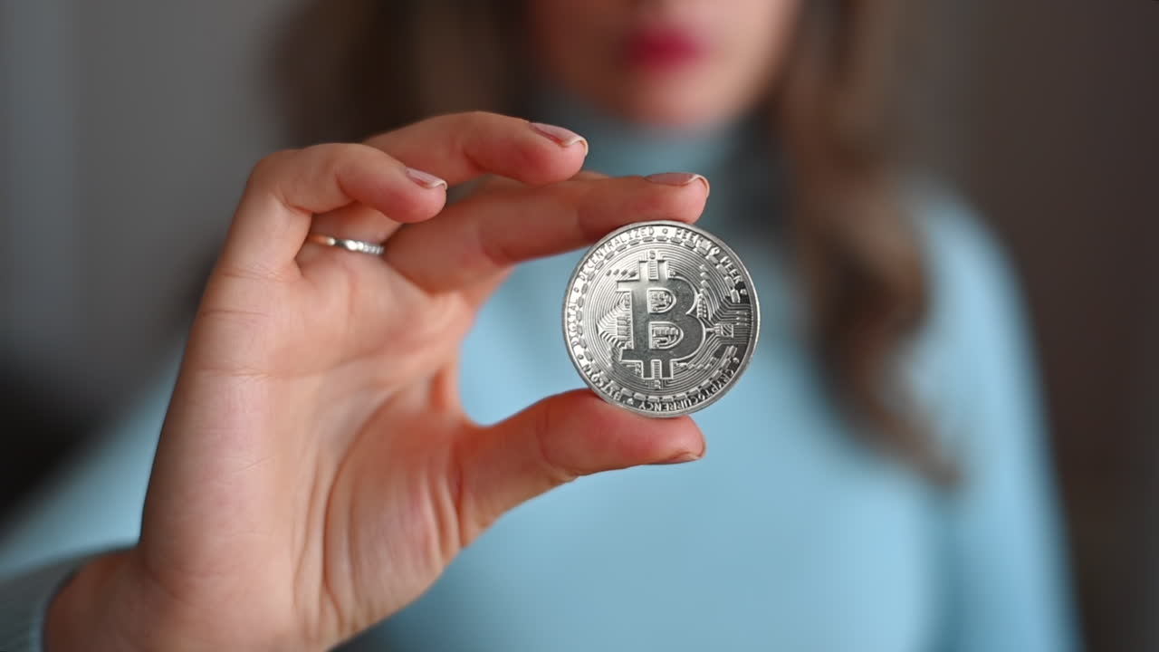 Brunette woman in a blue shirt holding a silver bitcoin