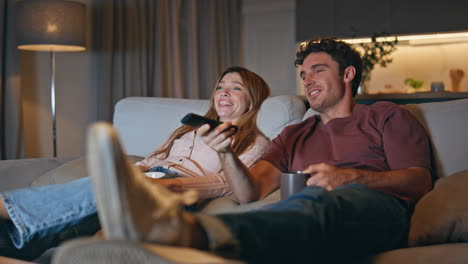 smiling spouses watching tv sitting at cozy living room interior late evening