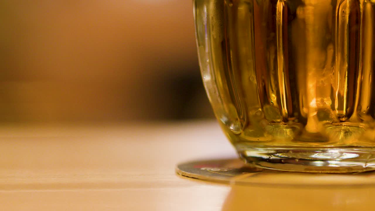 Golden lager beer poured into glass mug, warm ambient lighting, shallow focus, smooth camera movement