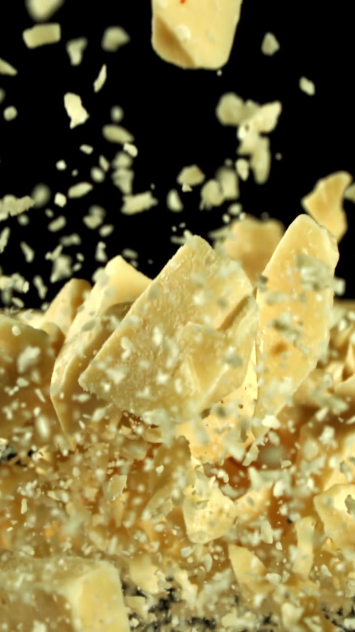 Slow Motion Falling Parmesan Cheese Pieces and Particles on Black Background