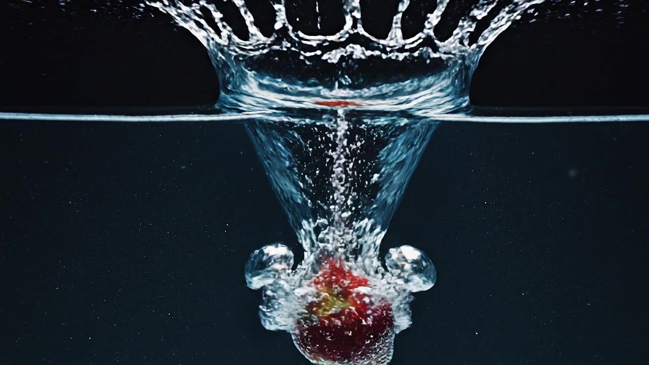 Red strawberry splashing into water against a dark background