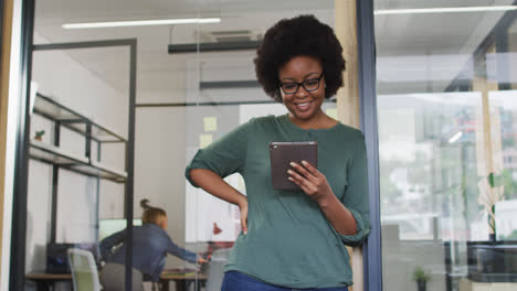 Empresaria-Afroamericana-Apoyada-En-La-Puerta-Usando-Una-Tableta-Sonriendo-A-La-Cámara-En-La-Oficina