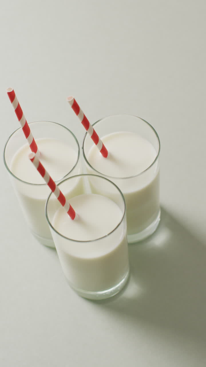 video vertical de tres vasos de leche con paja roja y blanca sobre fondo gris