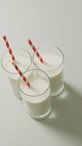 video vertical de tres vasos de leche con paja roja y blanca sobre fondo gris
