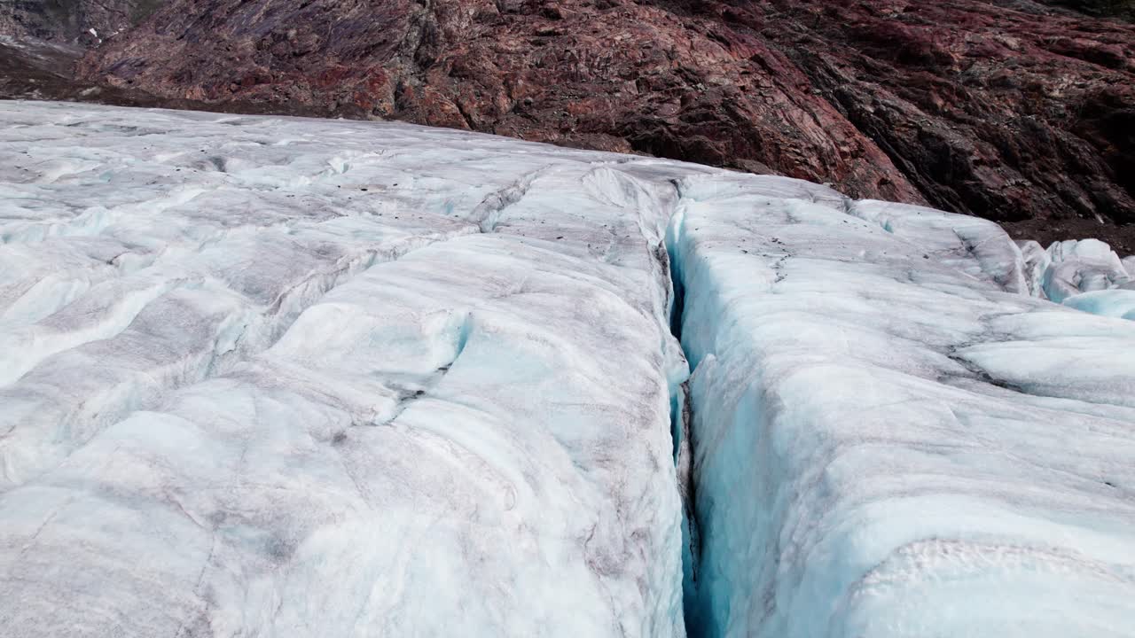 Filmische Luft-Nahaufnahme von gebrochenem Gletschereis, tiefblaue Gletscherspalten durchziehen uralte gefrorene Strukturen und offenbaren die rohe Kraft und Zerbrechlichkeit der alpinen Welt des Aletschgletschers in der Schweiz