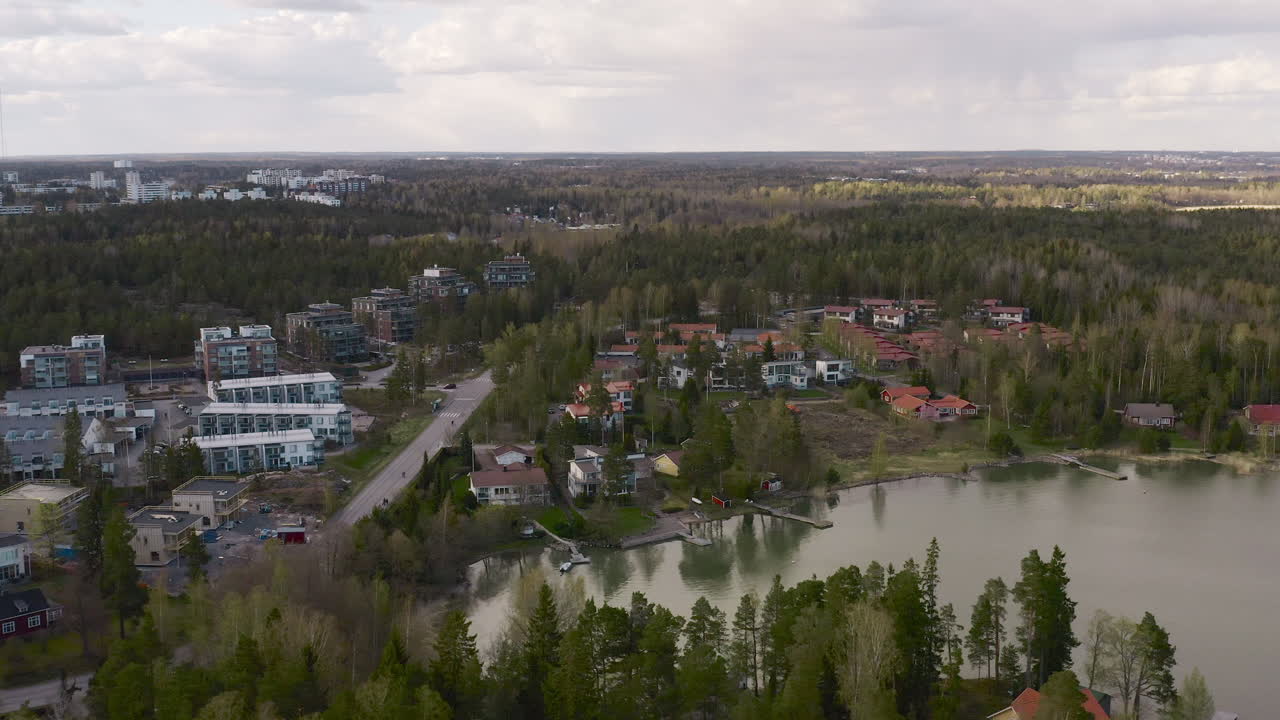 The main road leading into a town on the shore of a lake is revealed in an aerial view as it pans high above the thick forest