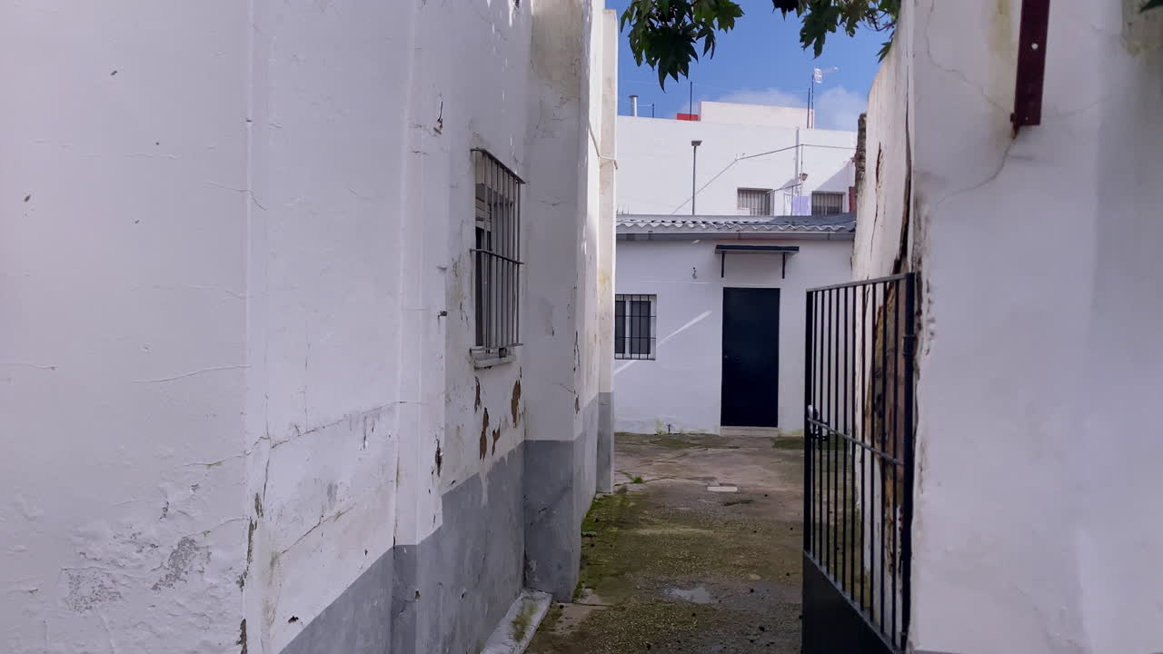 Stretto vicolo urbano a Sanlúcar de Barrameda, Spagna, che mostra vecchie pareti imbiancate a calce con pittura scrostata e un cancello aperto