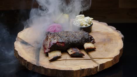 bbq ribs on a rustic wooden plate with pickles covered with a cloud of smoke - medium shot