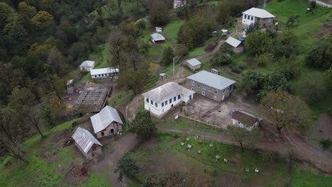 Aerial-orbits-school-house-in-small-village-on-steep-forest-slope