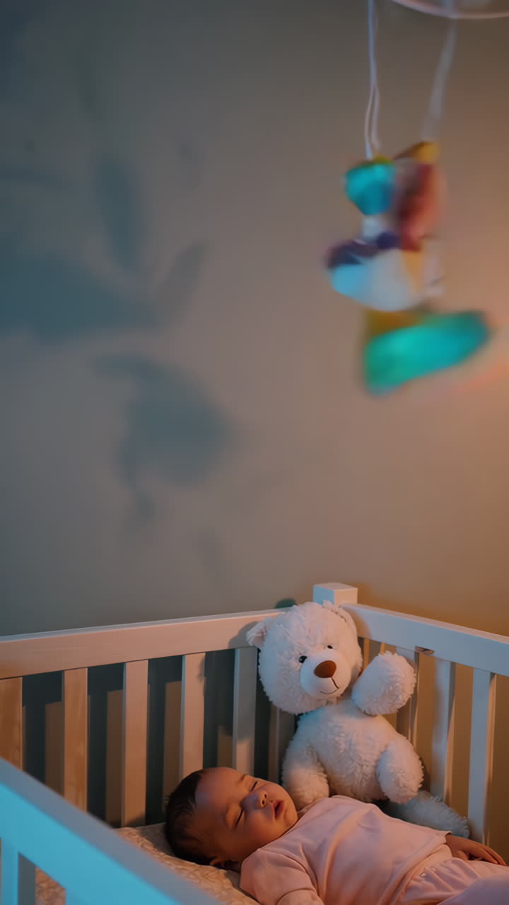 Bambino che dorme in una culla con giostrina e orsetto di peluche
