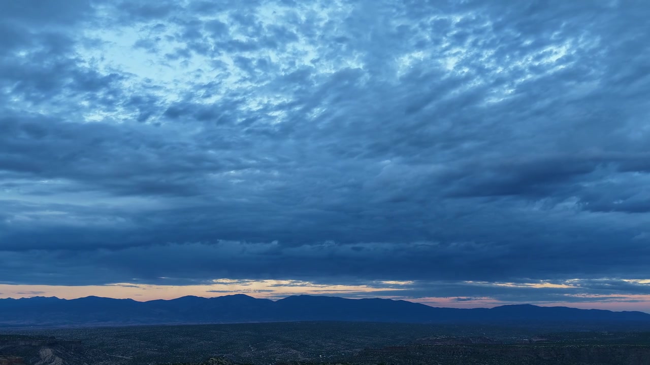 4K drone-timelapse af en fredfyldt blå time, der sænker sig over den store høje ørken i Santa Fe County, New Mexico. Tunge, teksturerede skyer driver over silhuetten af den fjerne Sangre de Cristo bjergkæde.
