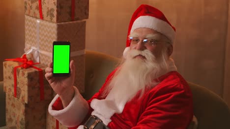 santa points his finger at the green screen mobile phone screen. christmas sale. elderly santa claus shows a screen with a chromakey