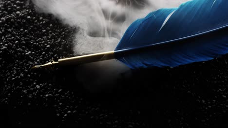 symbolic blue writing feather sits on black rocks as mythical smoke surrounds it