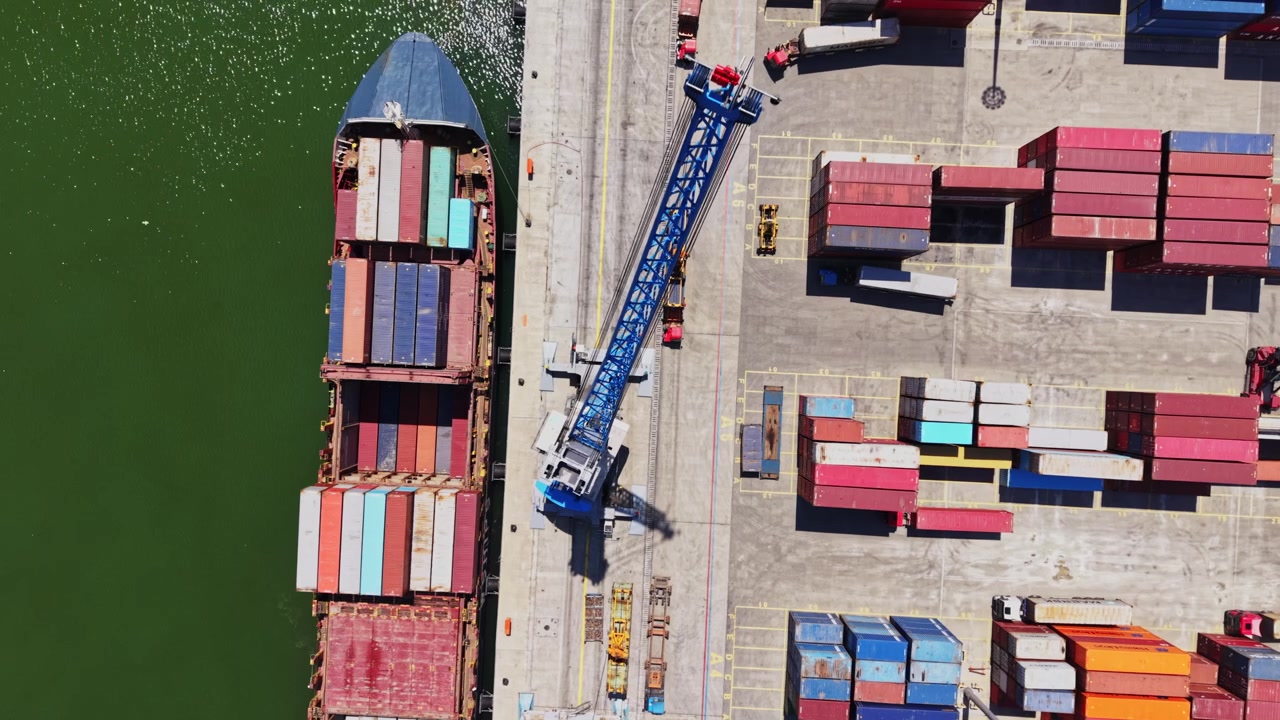 Frachtschiff am Dock mit Kran, der Container in einem geschäftigen Hafenbereich verlädt.